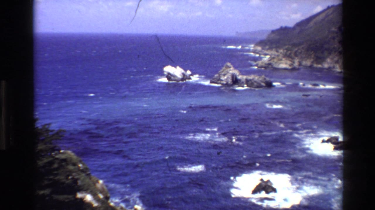 1980 8mm view of Big Sur, California, with deep blue water, white surf, offshore rocks, and coastal cliffs.