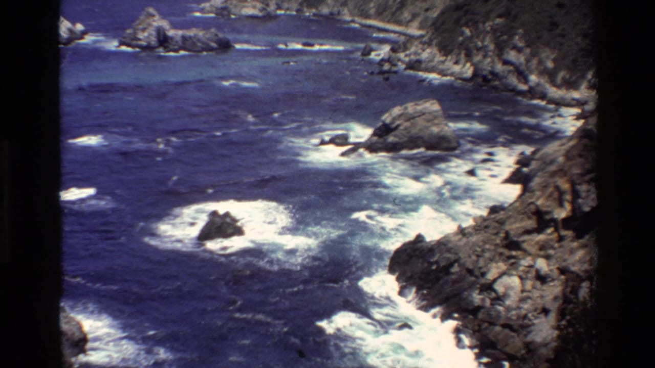 Rocky Big Sur coastline with blue ocean and white surf around offshore rocks.