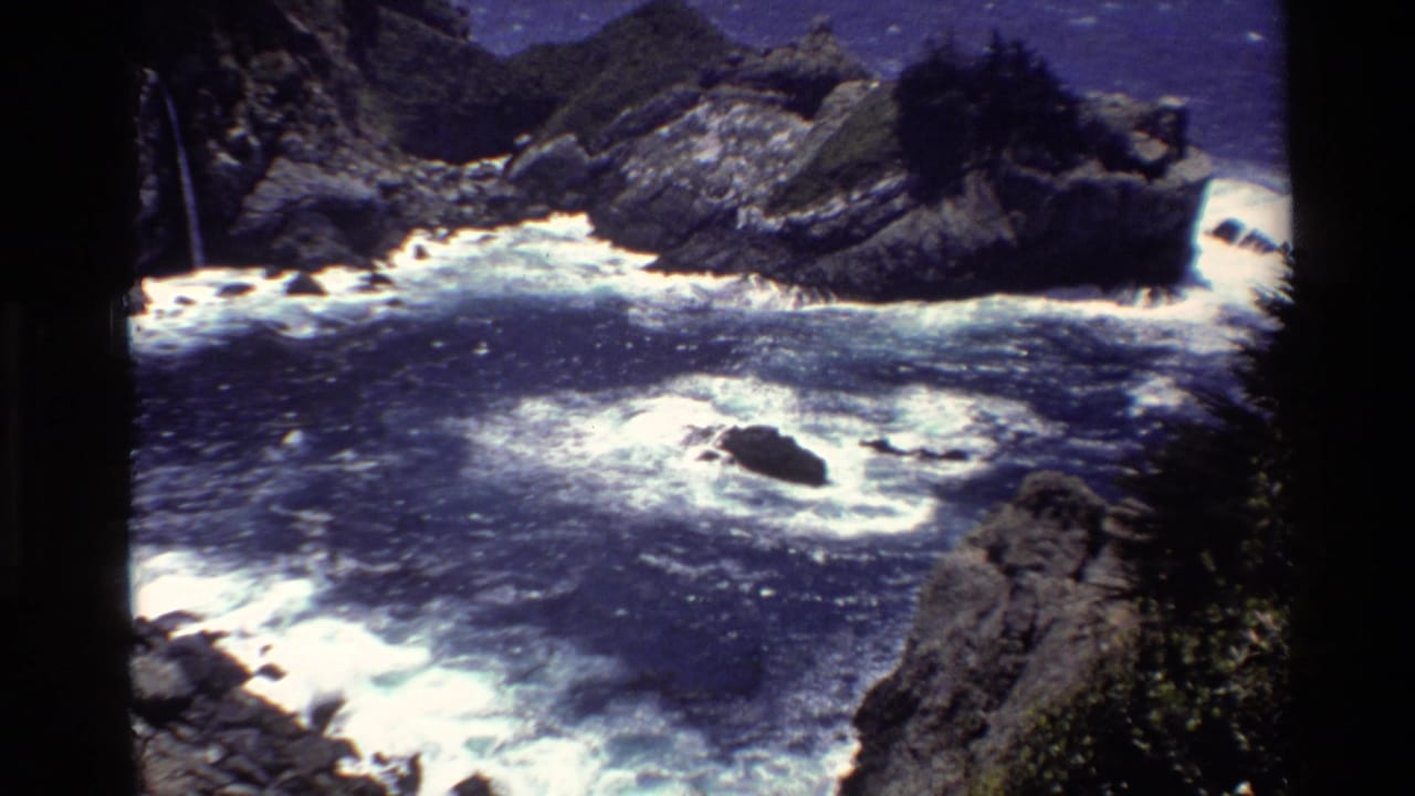 Big Sur coastal cutaway with rolling surf, jagged rocks, cliffside greenery, and bright midday light.