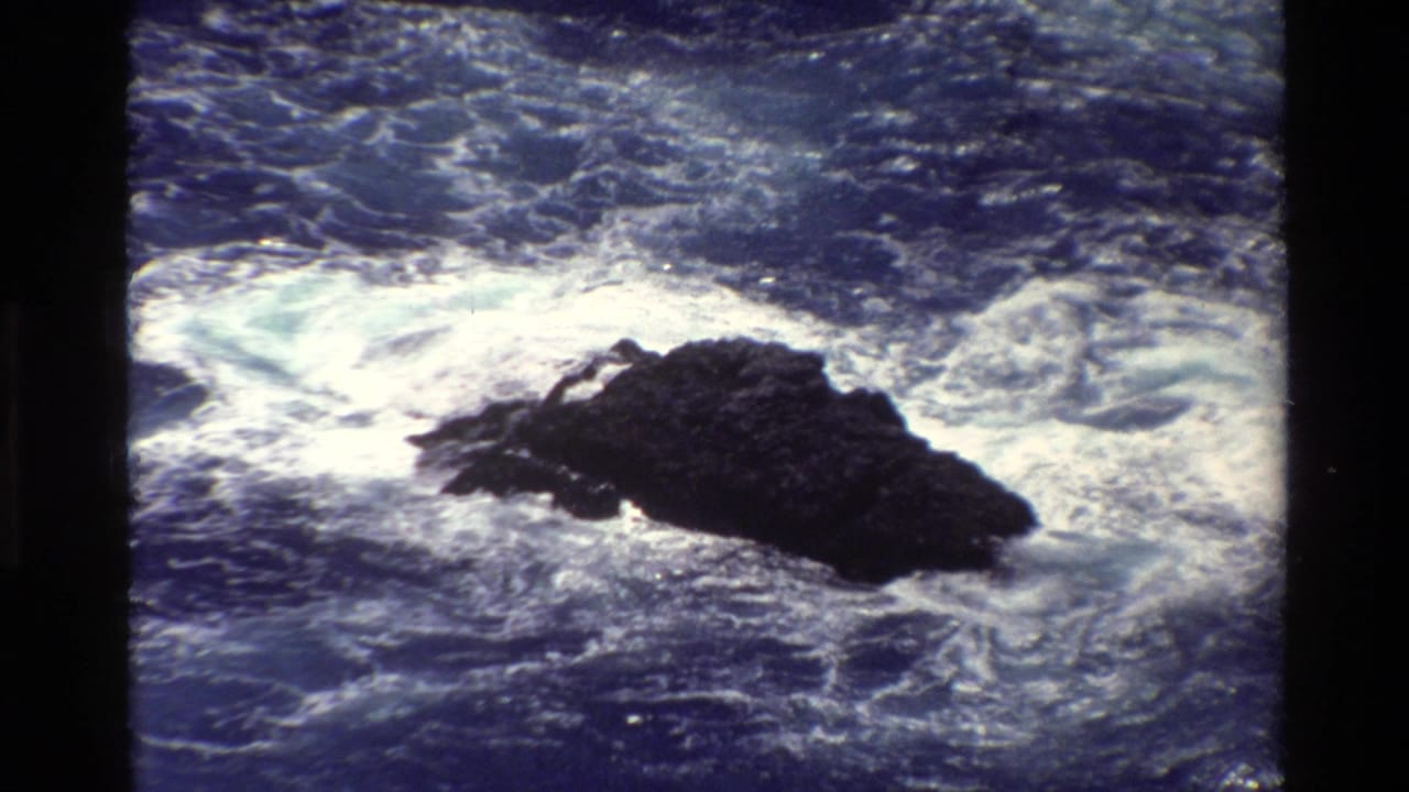 White surf breaks around a jagged rock in open water.