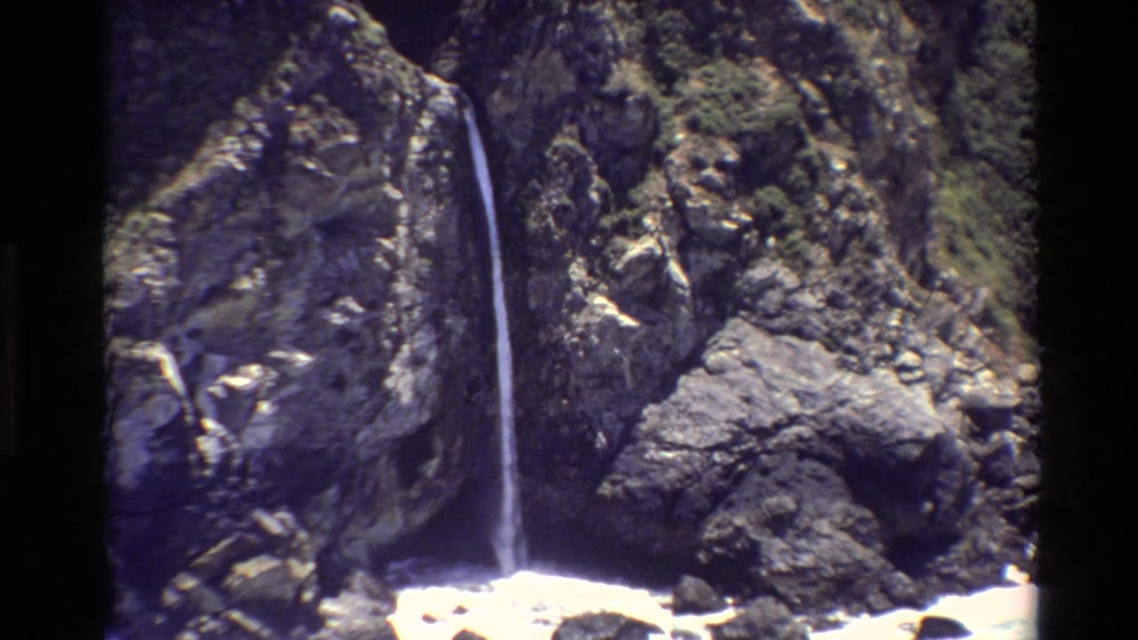 1980 Big Sur 8mm frame showing a thin waterfall falling through a rocky, moss-covered cliff area.