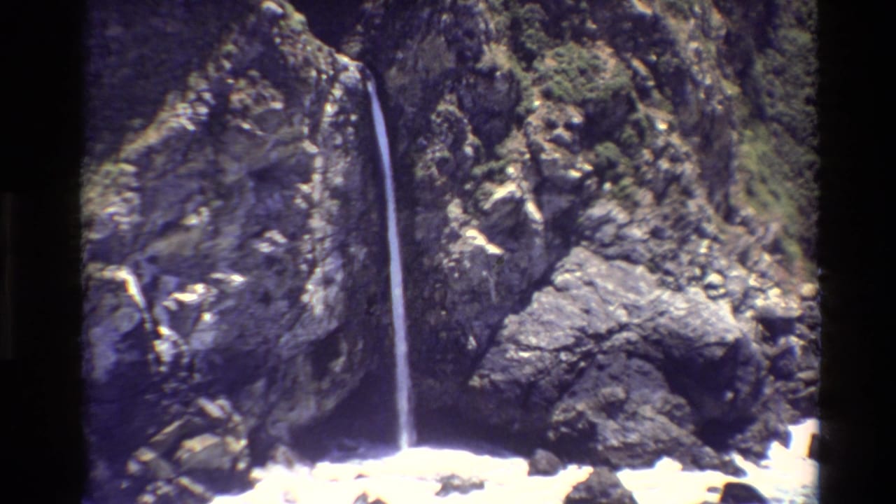 Waterfall continues down a steep rock face beside bright ocean foam.