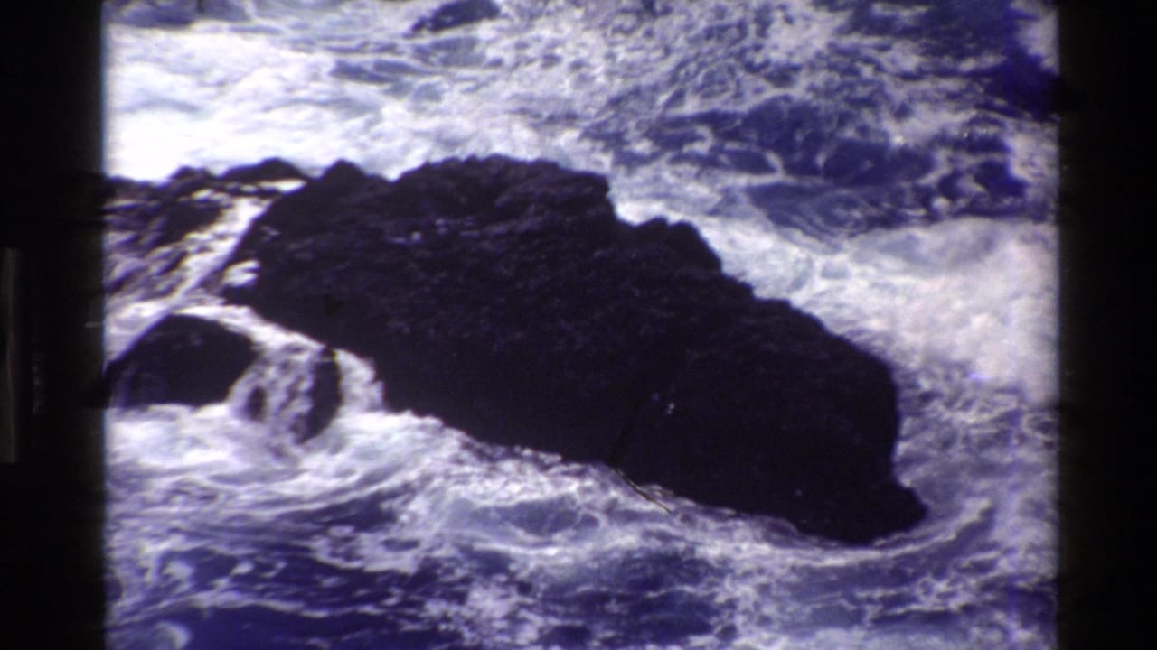 Dark rock surrounded by white surf and blue ocean water.