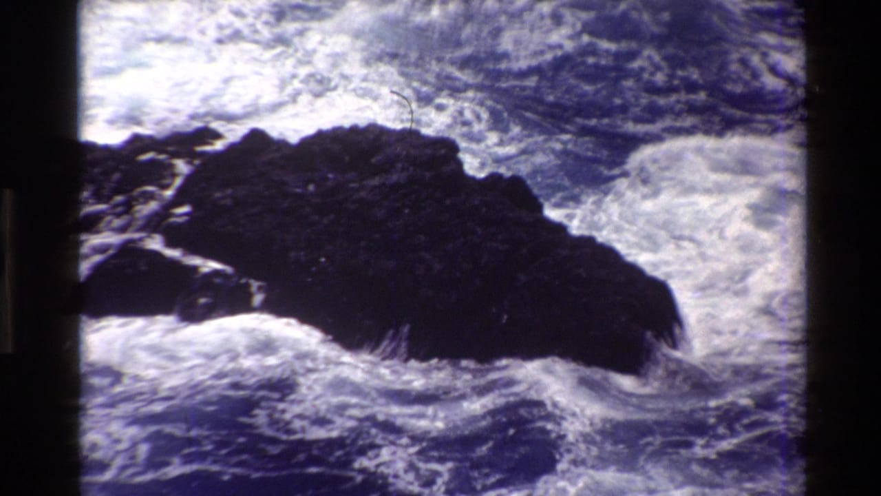 Foamy ocean water surges against a dark rocky outcrop.
