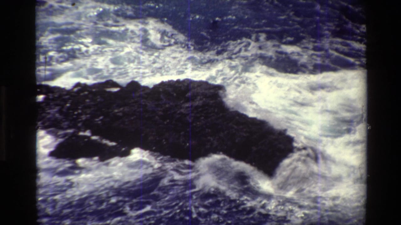 Foamy waves strike a long dark rock formation near the shoreline.