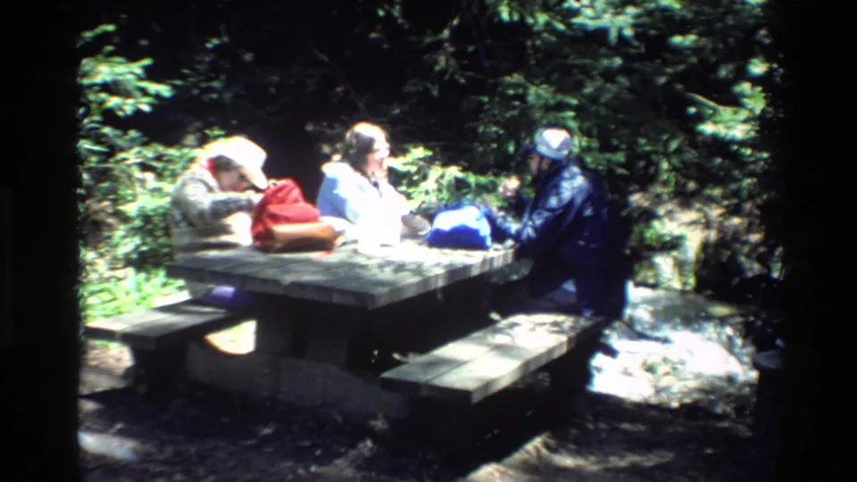 Family group seated at a wooden picnic table in sun-dappled Big Sur forest footage from 1980.