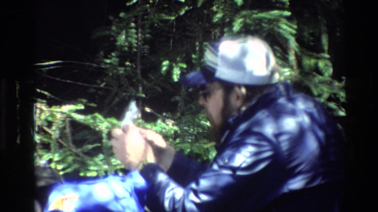 In 1980 Big Sur home-movie footage, a man in a white cap and dark jacket sits outdoors near food or small picnic items.