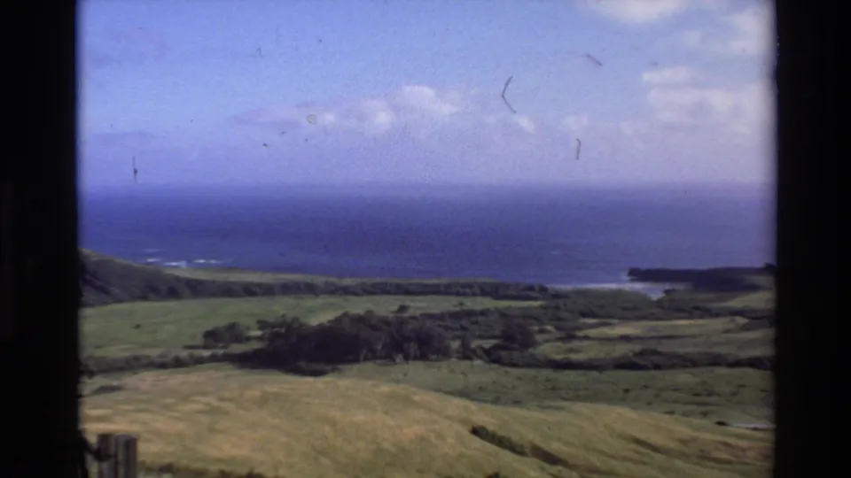 1980 Big Sur coastal view with rolling green hills, Pacific Ocean, blue sky, and distant headland in a soft 8mm frame.