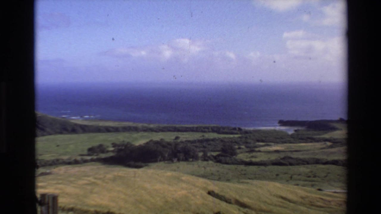 1980 Big Sur home-movie landscape showing grassy coastal hills, shoreline, ocean horizon, and lightly clouded sky.
