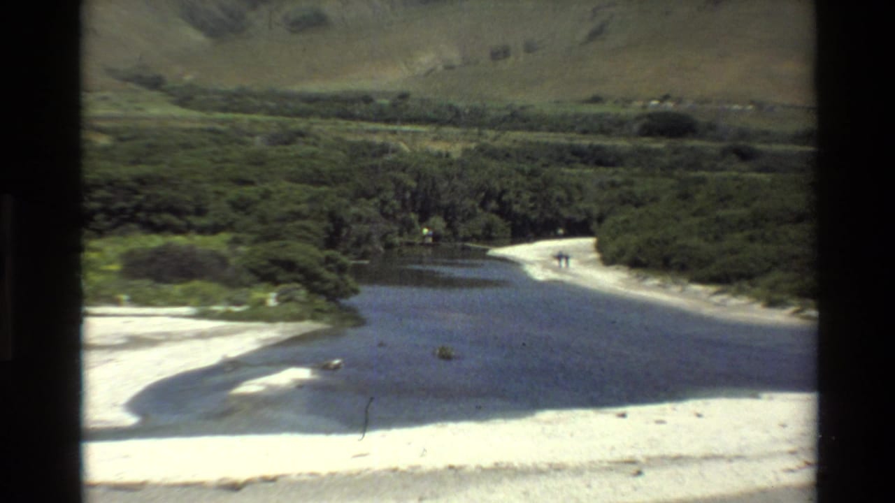 1980 Big Sur home-movie aerial view of a river or lagoon meeting a sandy beach below green hills and mountains.