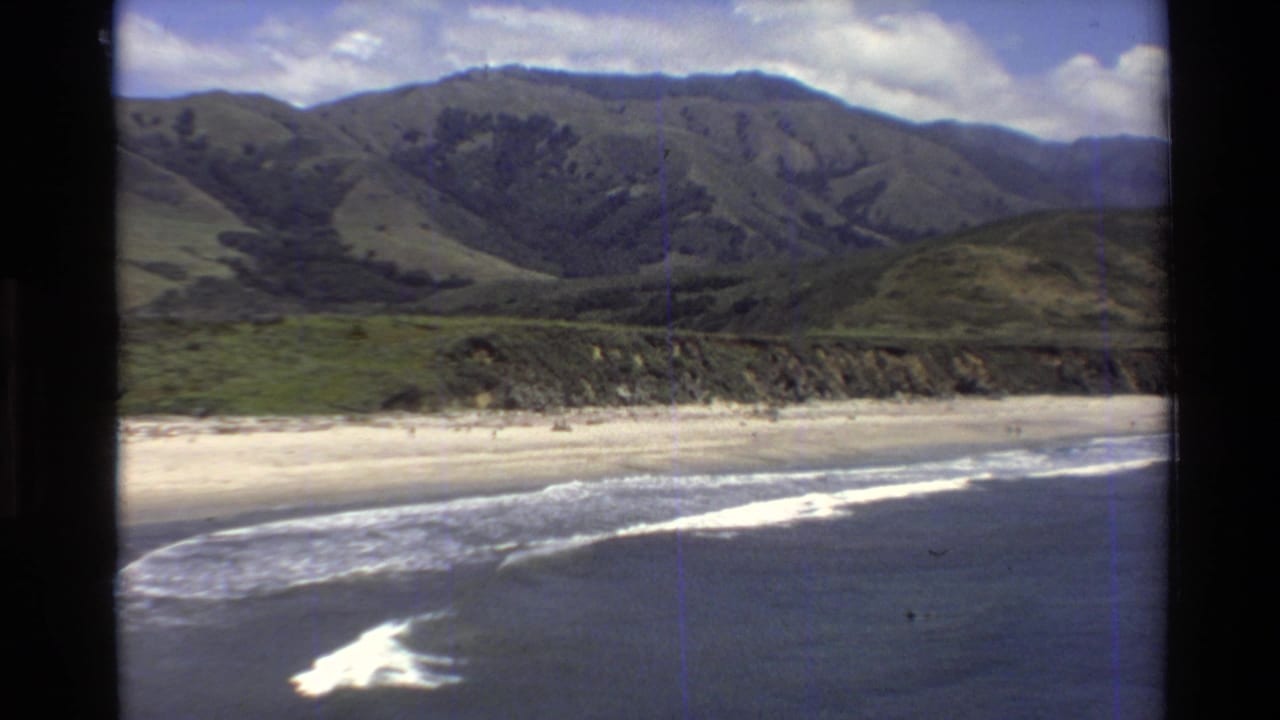 Foamy surf breaks near shore with mountains rising beyond the beach.