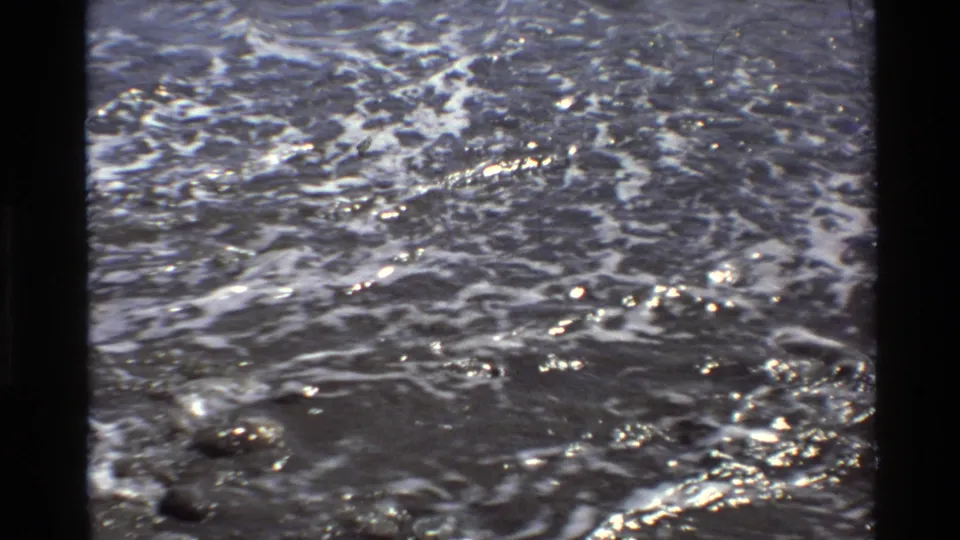 1980 Big Sur 8mm frame dominated by rippled ocean water with small foam streaks and glinting sunlight.