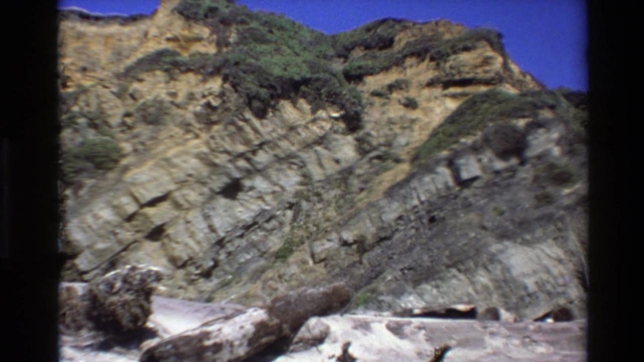 Rocky cliff face and beach driftwood under a clear blue sky.