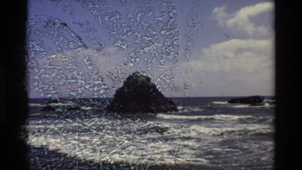 Big Sur 8mm frame with the sea stack, breaking waves, clouds, and prominent surface scratches across the scanned film.