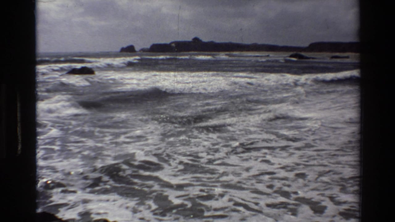 Vintage 8mm footage from Big Sur shows lower rolling surf, scattered rocks, and a dark headland across the horizon.