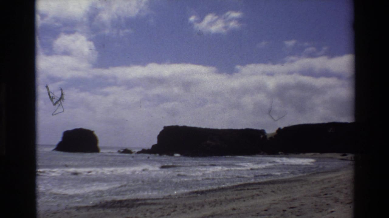 Rocky coastal scene with sea stacks and surf; film debris scratch marks visible across the upper portion of the frame.