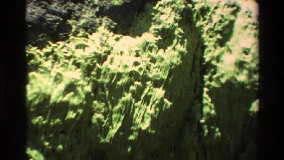 Super 8 film frame circa 1980 showing a lichen-encrusted Big Sur rock face at moderate zoom with dark film-gate borders visible.