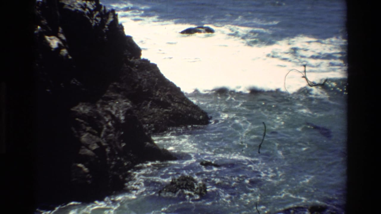 Rocky Pacific coastline, likely Big Sur, California, circa 1980 — 8mm home movie frame showing waves breaking against dark coastal rocks.