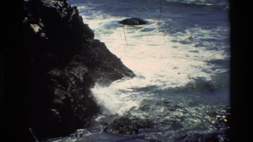 Pacific coastline, circa 1980, likely Big Sur — 8mm home movie showing dark rocks and breaking surf with characteristic film grain and vignetting.