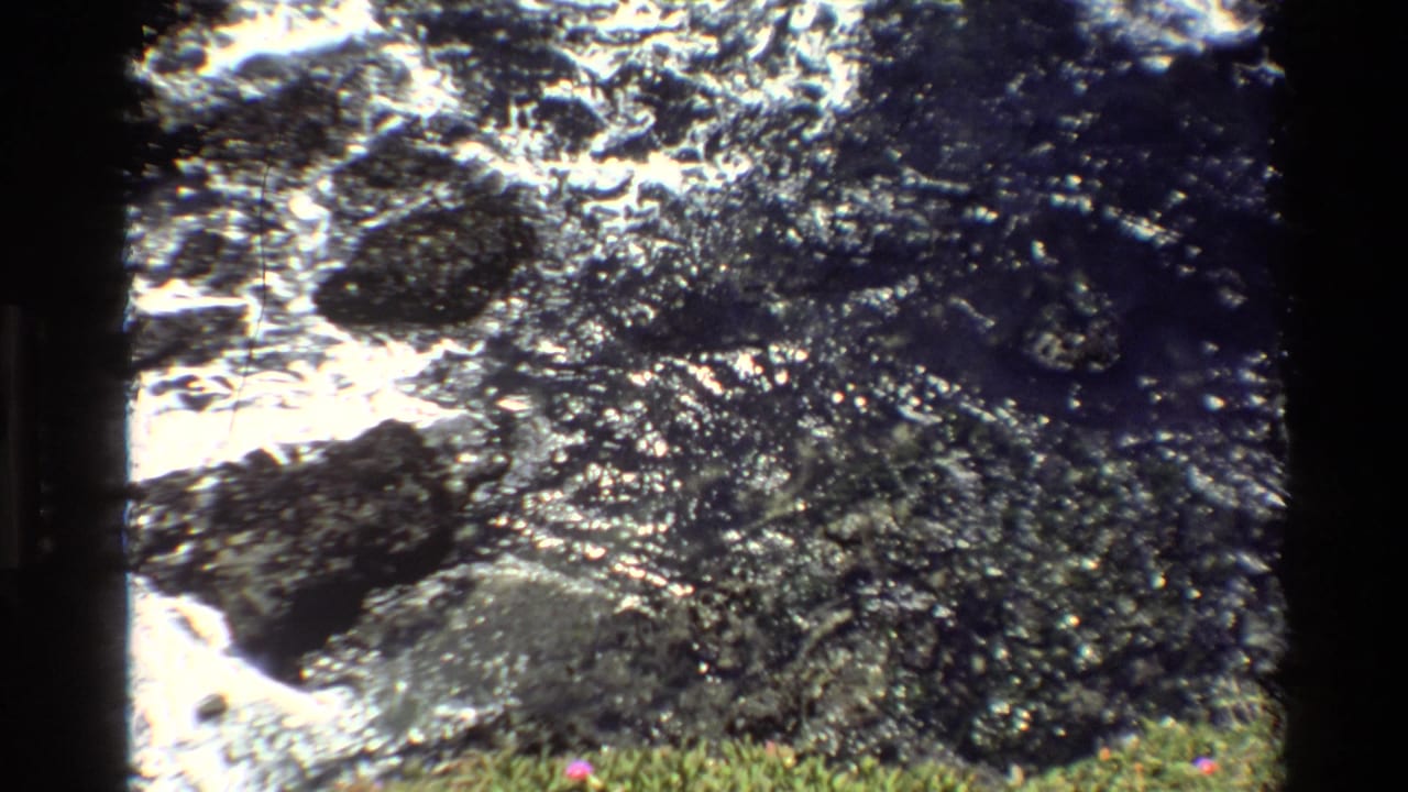 Super 8 home movie, circa 1980, Big Sur, California — churning white water over dark rocks with sunlit sparkle and grassy foreground.