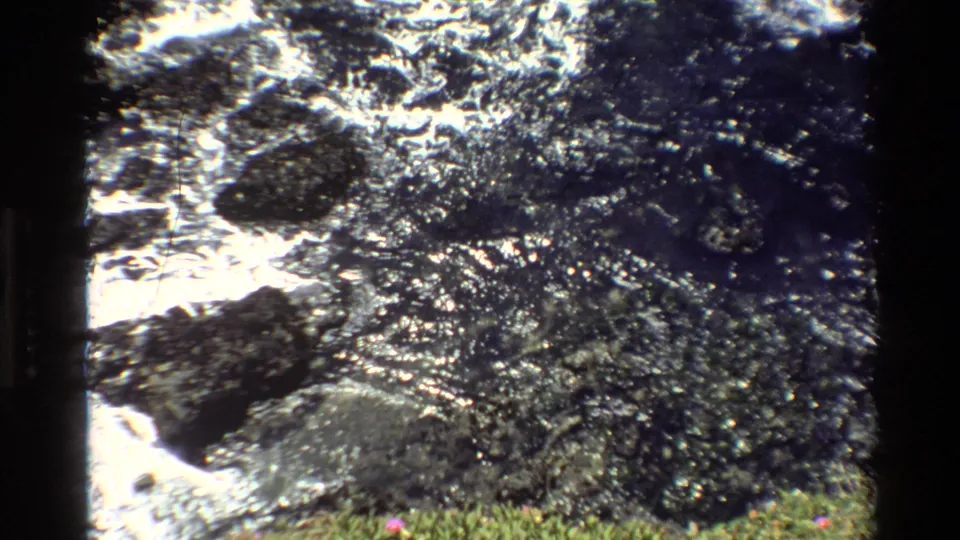 Super 8 home movie, circa 1980, Big Sur, California — churning white water over dark rocks with sunlit sparkle and grassy foreground.