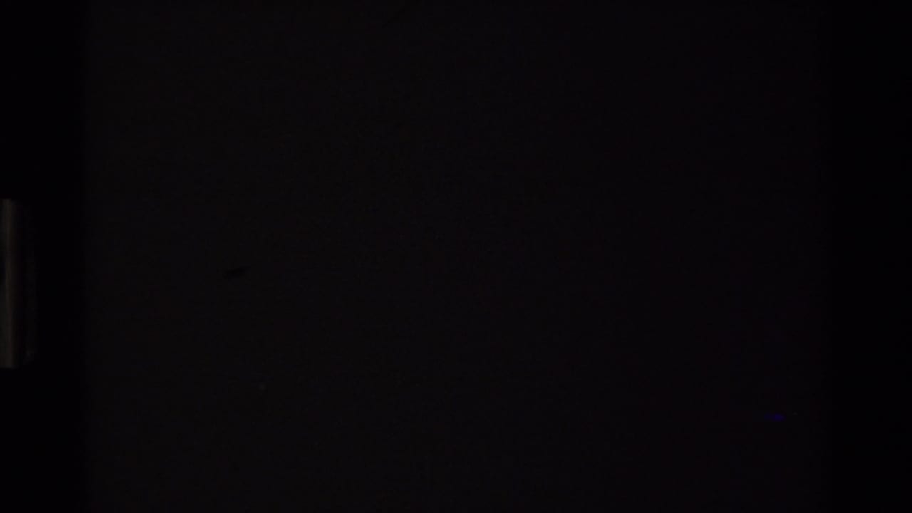 Dark 8mm film leader circa 1980 showing near-total exposure darkness with a faint blue-green light leak at center, preceding the landscape footage.