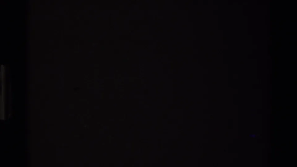 Dark 8mm film leader circa 1980 showing near-total exposure darkness with a faint blue-green light leak at center, preceding the landscape footage.