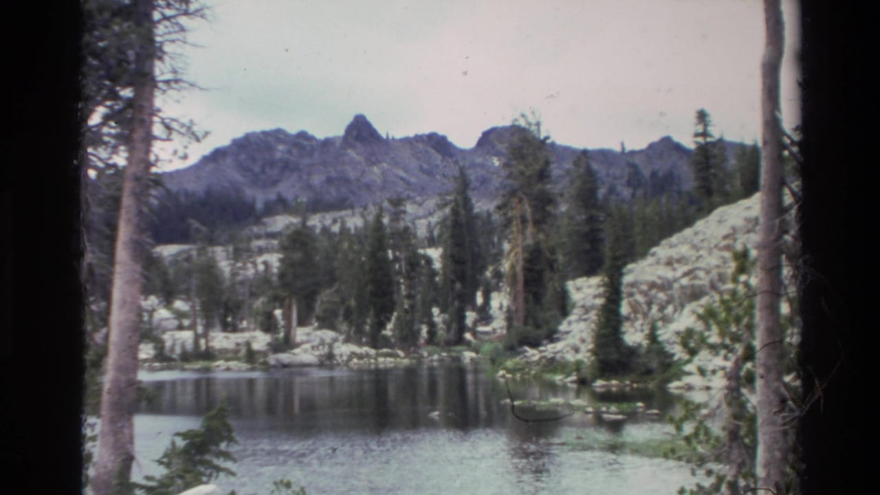 Alpine lake with conifer treeline and granite peaks, Big Sur area, California circa 1980, captured on 8mm home-movie film with grain and colour fading.