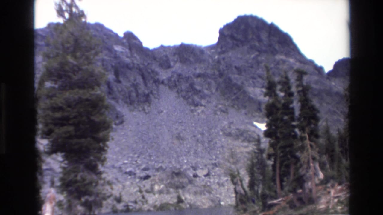 Talus-covered mountain slope with tall conifers and jagged peaks, California mountain area circa 1980, 8mm home movie