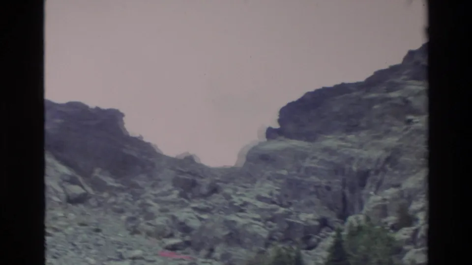 Close-up pan of a steep rocky mountain face with conifers at its base, Big Sur area, California, c. 1980, with pinkish Super 8 color cast.
