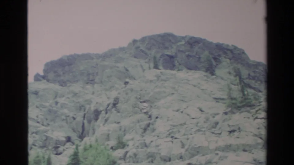 A broader rocky ridge with scattered conifers and scrub vegetation, Big Sur area, California, c. 1980; Super 8 pinkish-mauve color cast visible.