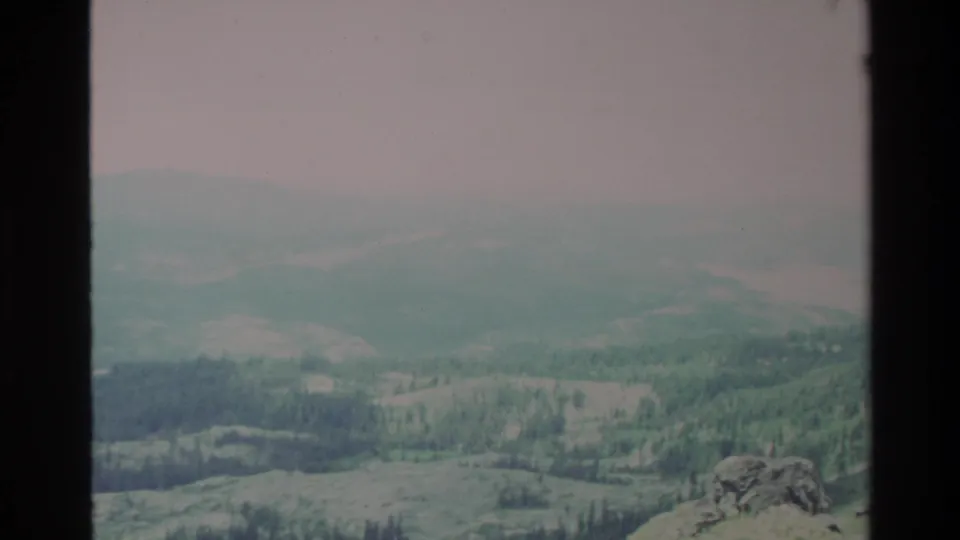 Wide valley vista with layered green forested ridges fading into haze, Big Sur area, California, c. 1980; Super 8 teal-green and pinkish tones.