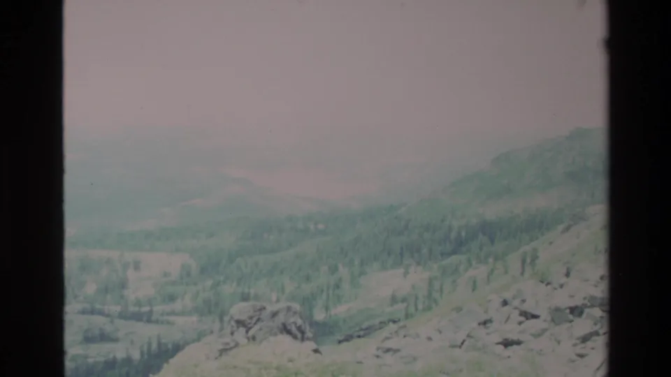 End frame of a slow pan across an apparent Big Sur-area ridge in 1980s 8mm home movie; rocky outcrops, conifer forest, and hazy overcast sky.
