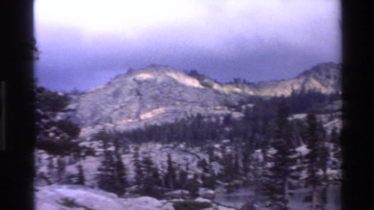 Same mountain and forest view after a slight camera pan right, overcast sky, Super 8 footage circa 1980.