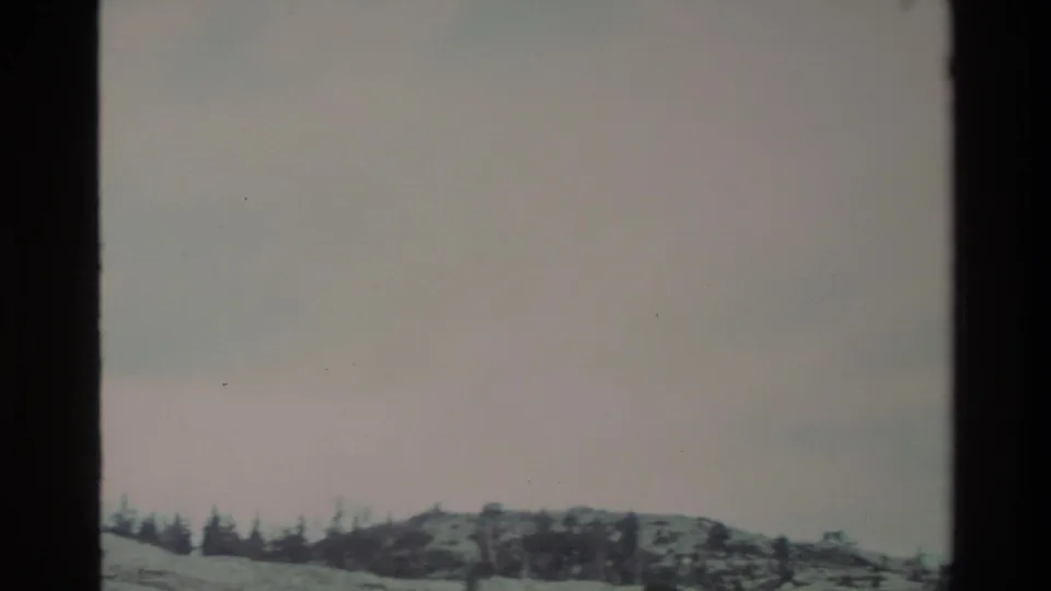 8mm frame near end of upward pan: open pale sky dominates with a slender snowy ridge and sparse conifer treeline at the bottom, California backcountry circa 1980.