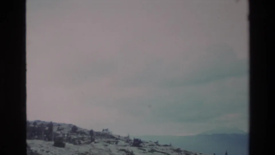 The same snow-dusted ridge slightly panned, revealing distant blue-gray hills; Big Sur highlands, California, circa 1980, 8mm film.