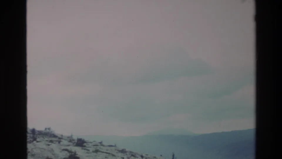 Broad snow-covered slope and expansive overcast sky as the camera tilts down; Big Sur highlands, California, circa 1980, 8mm film.
