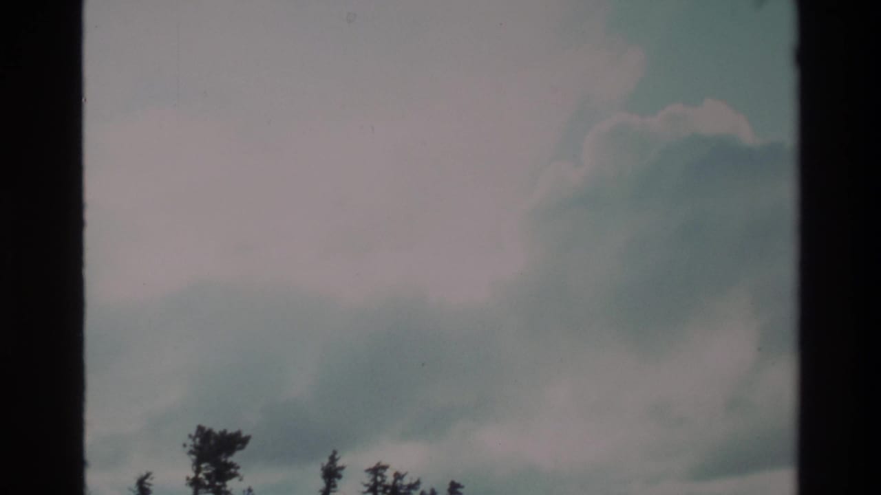 Super 8 wide shot of a cloud-filled sky over a rugged shrub-dotted hillside, consistent with California coastal uplands, circa 1980.