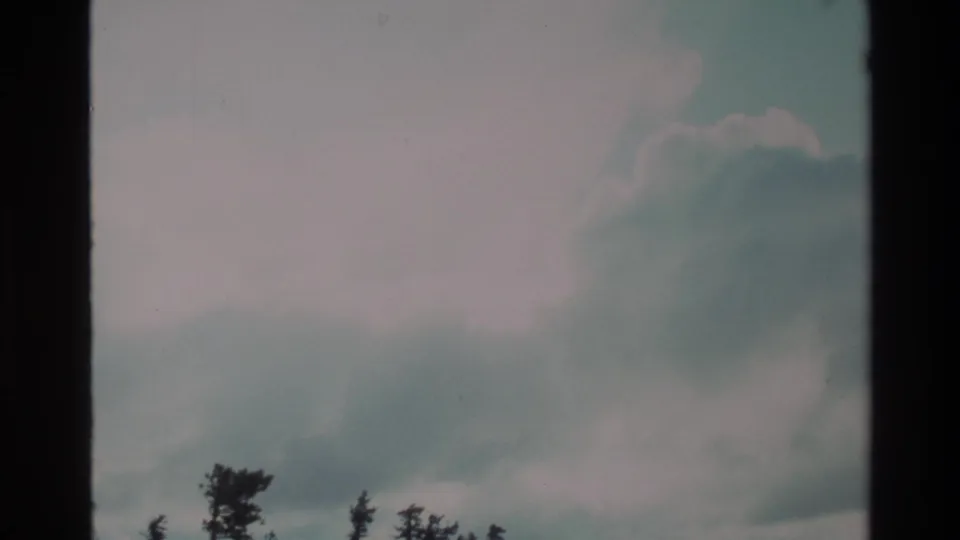 Super 8 wide shot of a cloud-filled sky over a rugged shrub-dotted hillside, consistent with California coastal uplands, circa 1980.