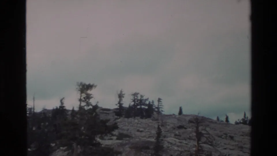 Super 8 shot of a rocky ridgeline with windswept sparse conifers under an overcast sky, consistent with Big Sur uplands terrain, circa 1980.