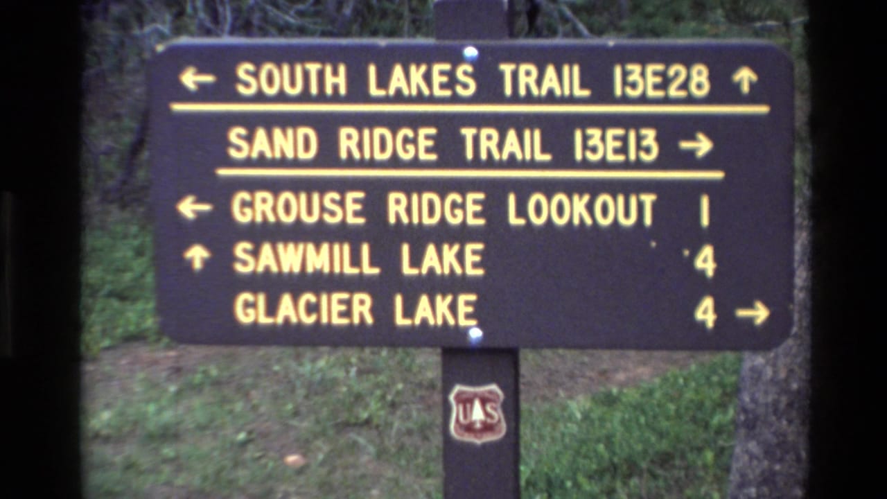 Brown trail sign with yellow lettering pointing to South Lakes Trail and nearby destinations.