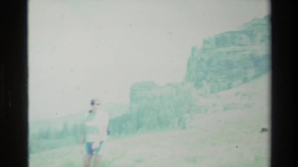 Distant hiker in light clothing on a sunlit Big Sur hillside, with pale mountain ridges behind them in faded 8mm color.