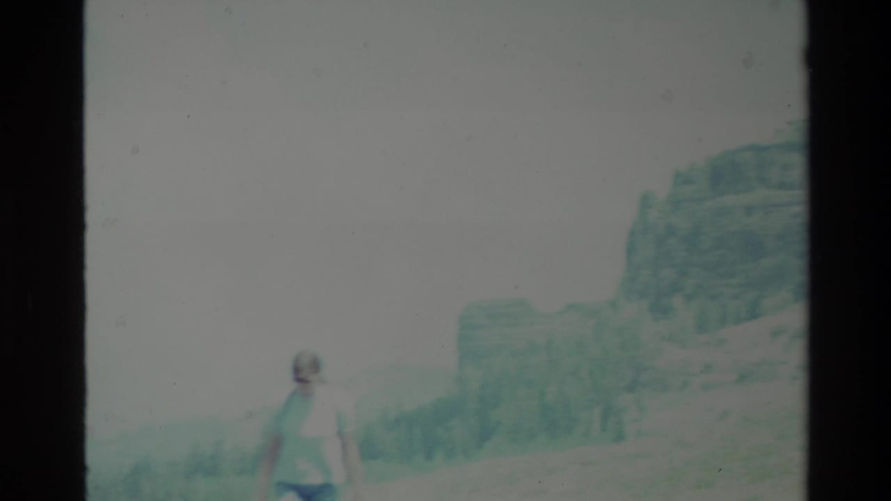 Woman in a light top stands near a pale mountain valley with dark film borders.