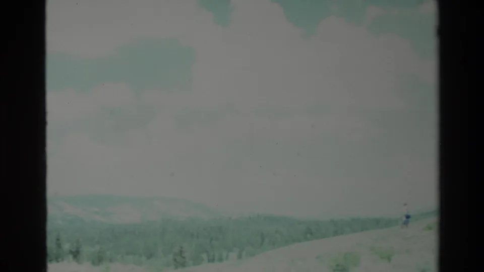 Big Sur home-movie frame with a small distant person on a hillside overlooking forested terrain.