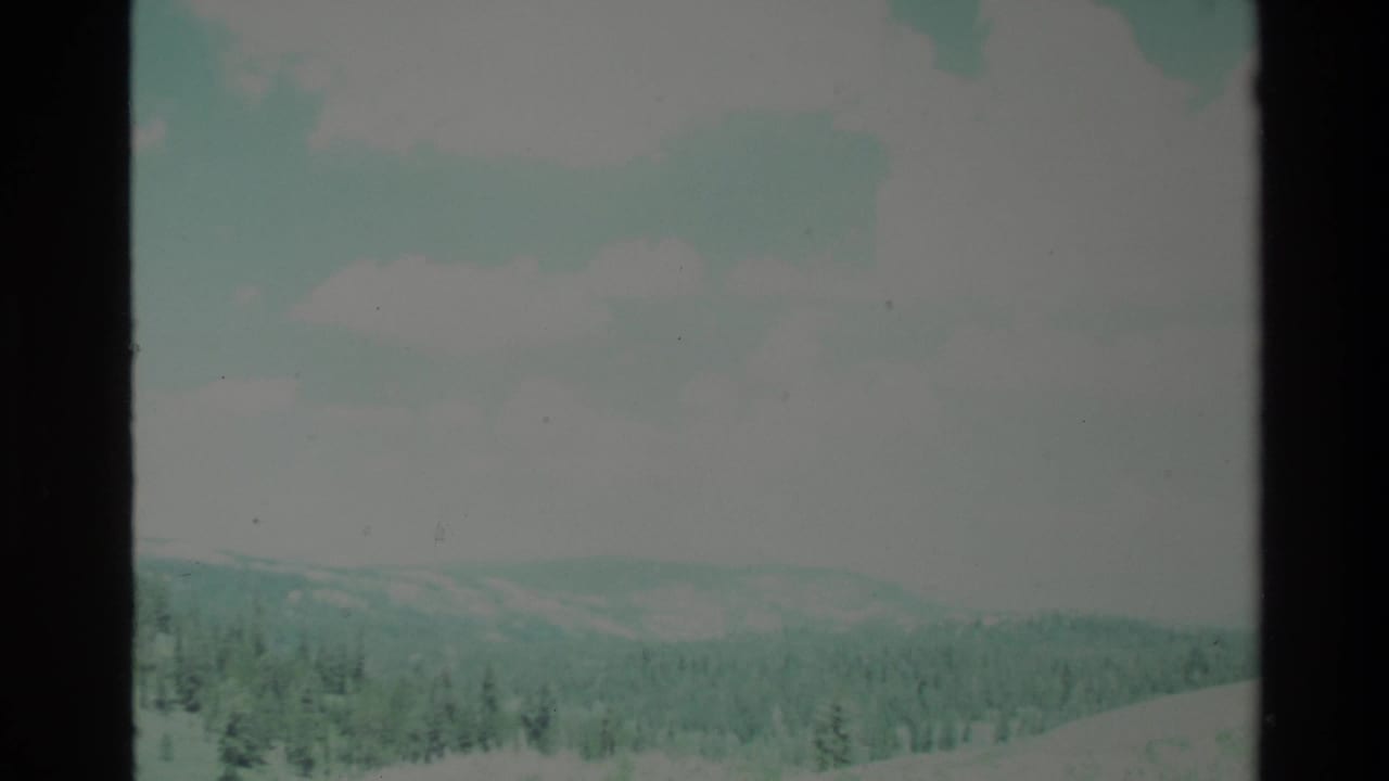 Wide 1980 Big Sur landscape view on 8mm film, with hazy ridges, a tree line, pale clouds, and visible contact-sheet border artifacts.