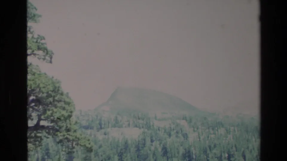 Soft 1980 Big Sur 8mm view of forested hills and a rounded distant hill under pale exposure.