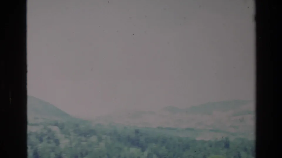 1980 Big Sur 8mm frame showing a pine-covered valley with hazy mountain ridges under a pale sky.