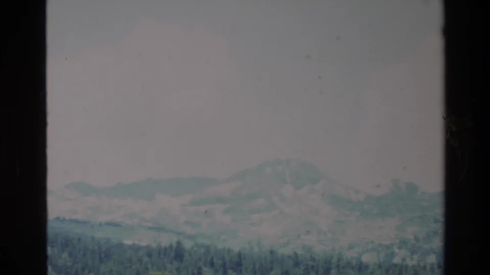 Faded 1980 Big Sur 8mm frame showing muted mountains and a dark pine forest foreground.