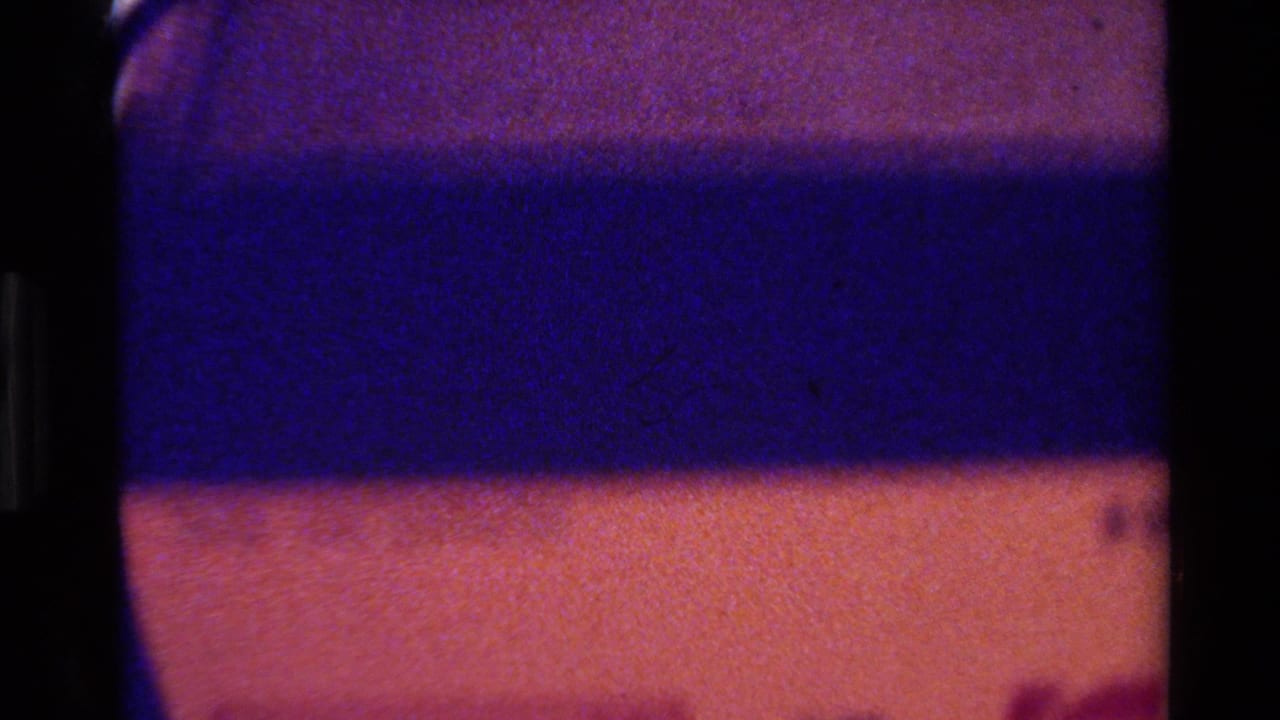 1980 Big Sur 8mm close-up showing part of a likely red dumbbell or cylindrical object against a blue-purple banded surface.