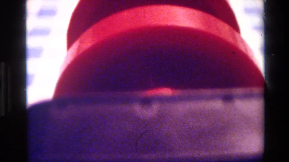 1980 Big Sur home-movie frame showing likely red dumbbell ends or stacked cylindrical forms with a dark band across the foreground.